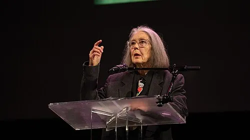 Anne Carson speaks at a lectern during a reading