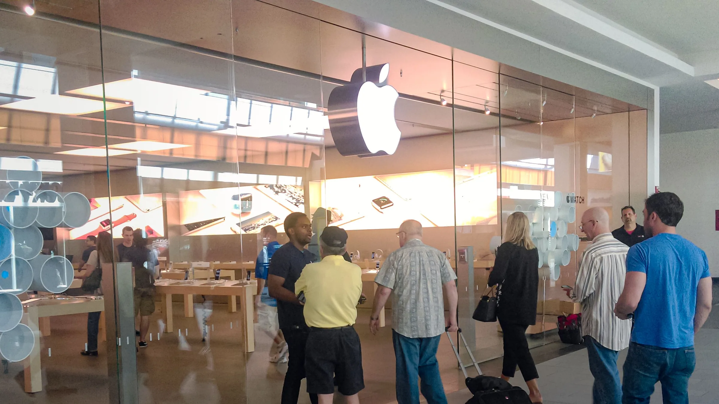 Shoppers outside an Apple Store with the Apple logo on the glass