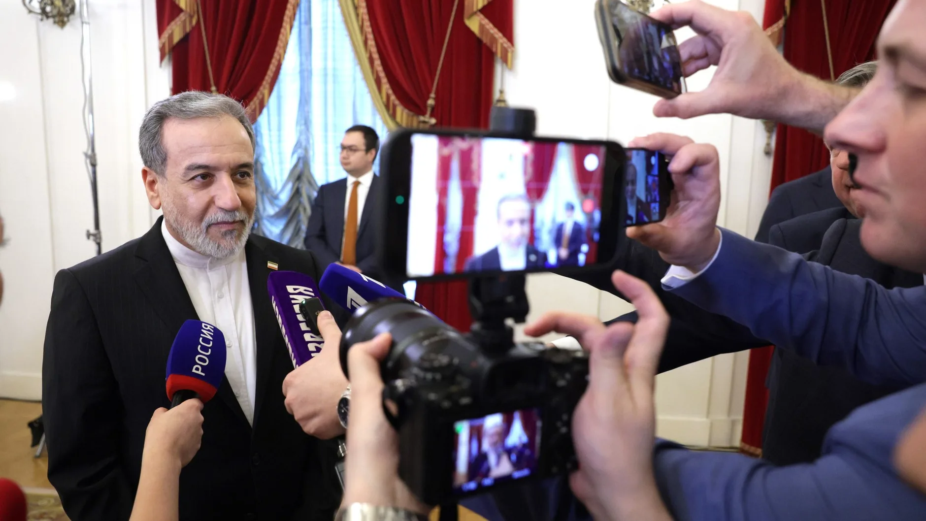 Iranian Foreign Minister Abbas Araghchi speaks to reporters holding microphones and phones