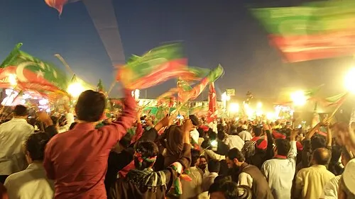 PTI supporters wave red and green party flags at a night rally