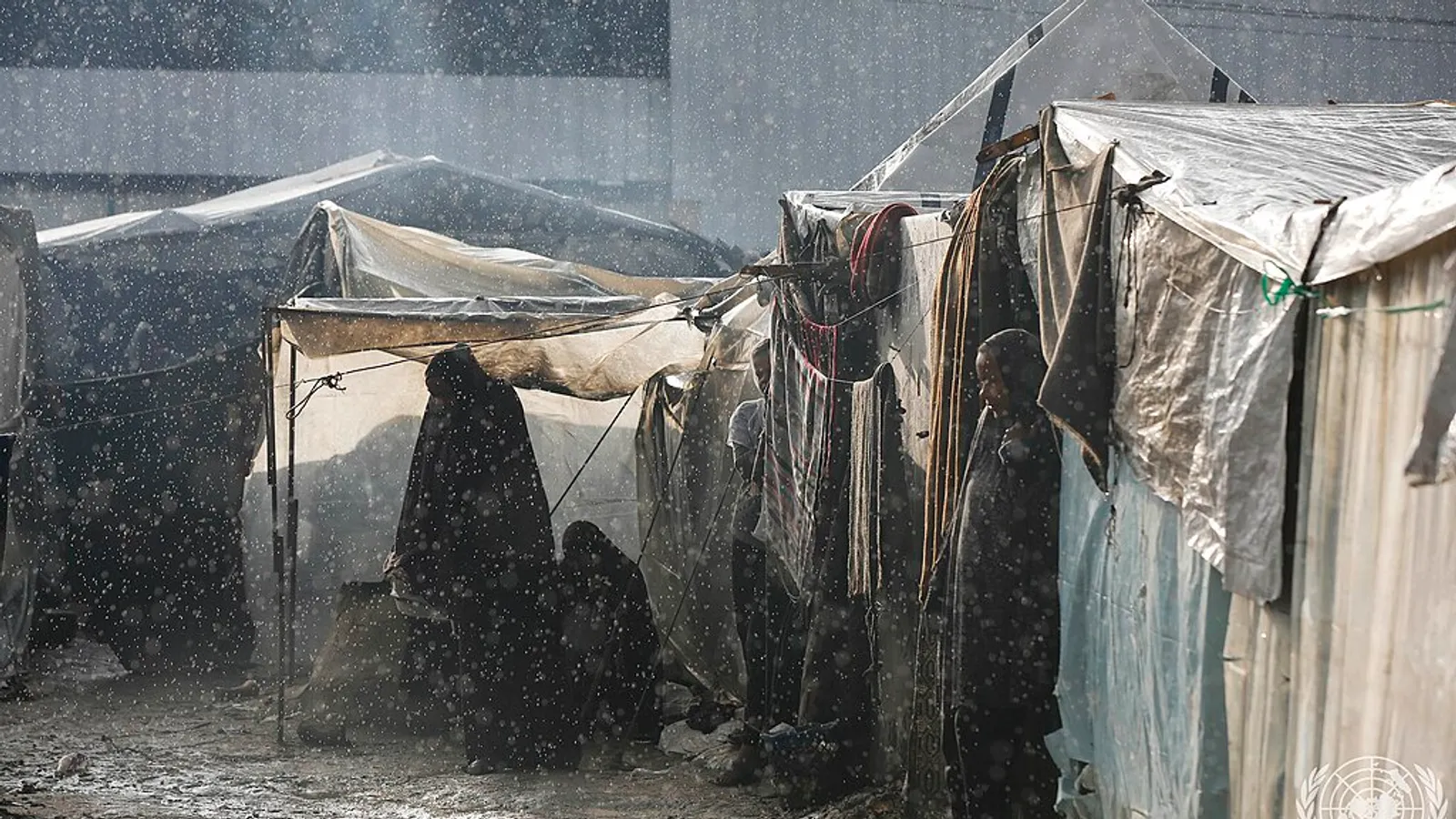 Displaced Palestinians walk among flooded tents in the rain in Deir el-Balah