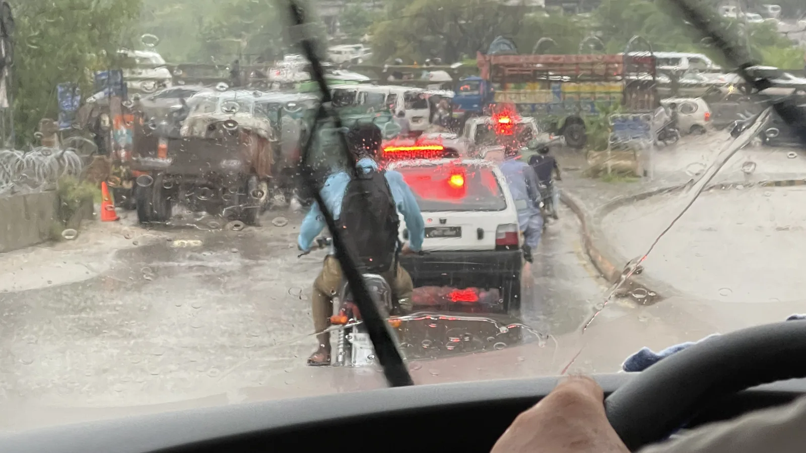 Traffic and a motorcyclist on a rain-soaked road in Islamabad, seen through a car windscreen