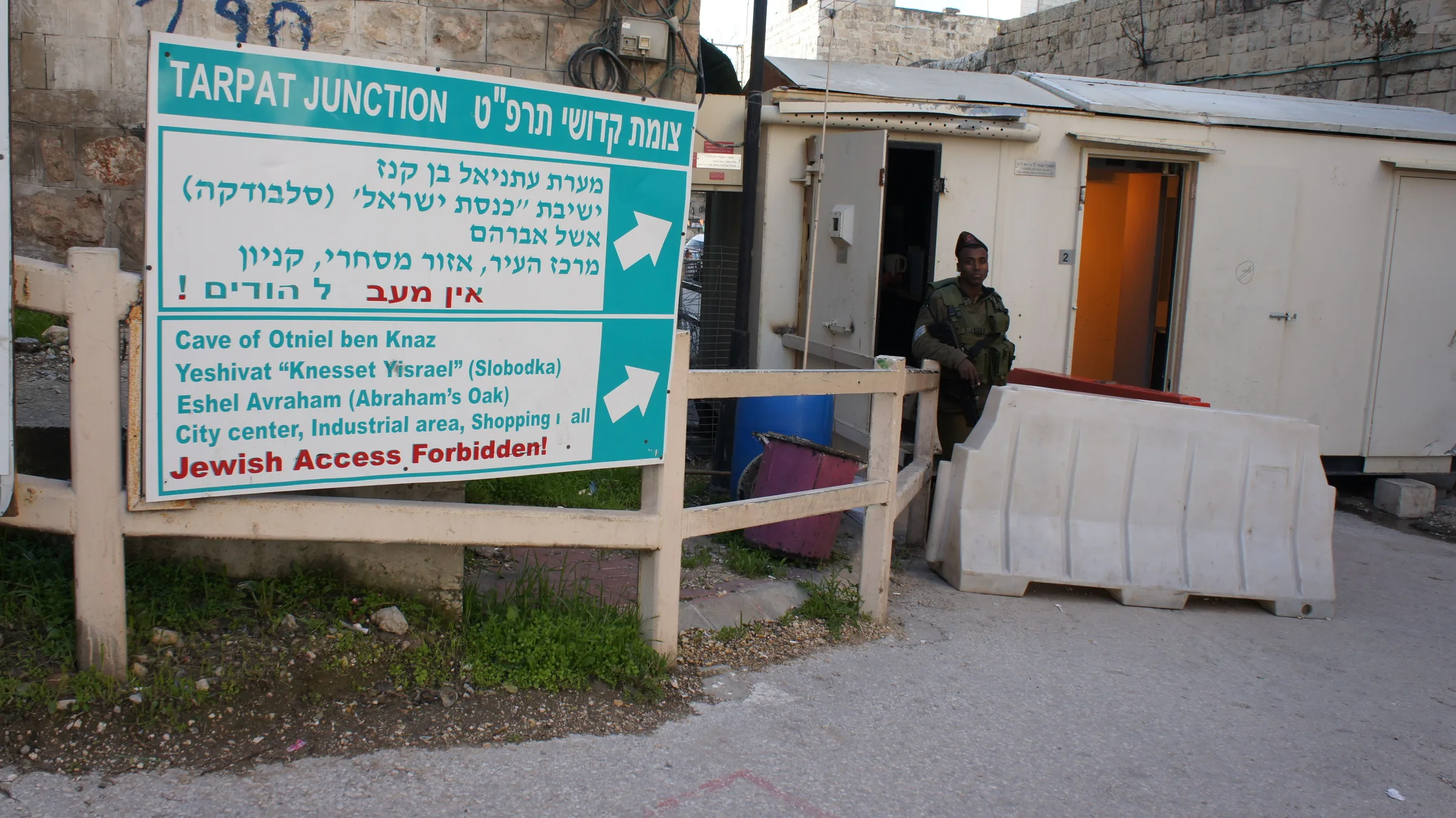 An Israeli checkpoint at Tarpat Junction in Hebron with a soldier beside a road sign