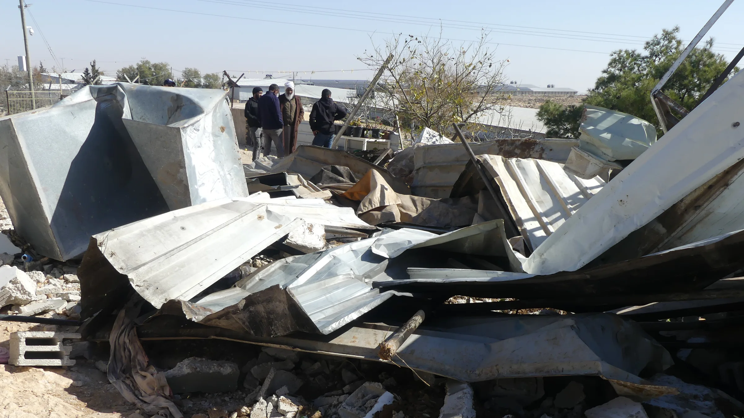 Rubble of demolished structures with people standing nearby in the occupied West Bank