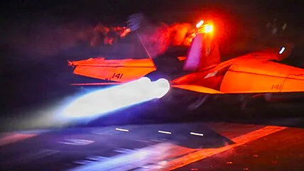 A fighter jet launches at night from the deck of the aircraft carrier USS Abraham Lincoln