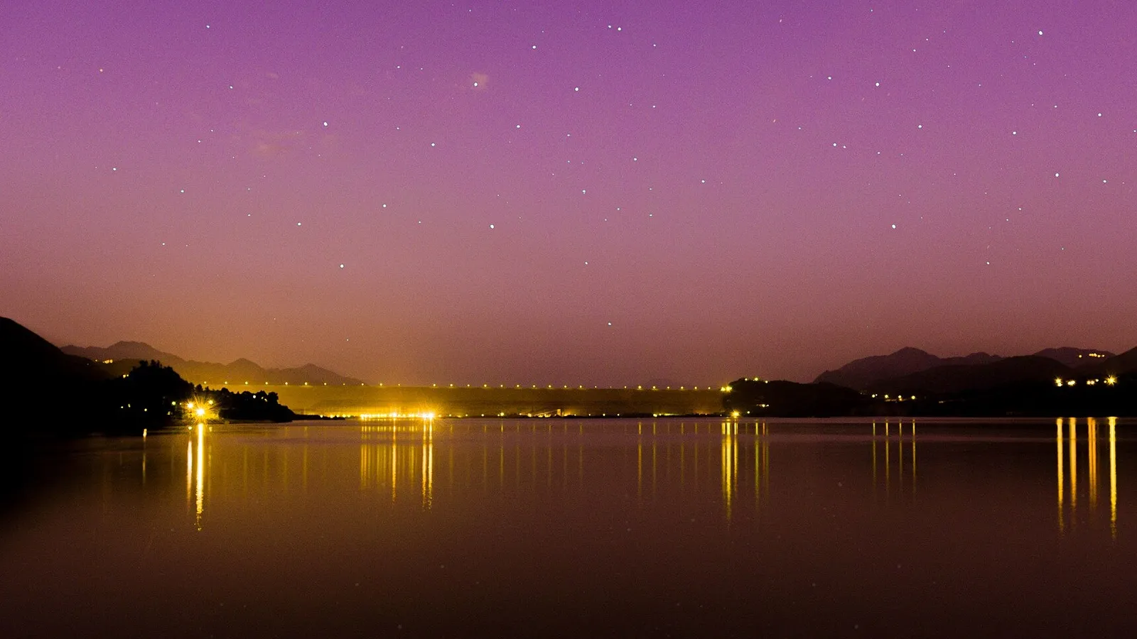 Tarbela Dam's reservoir on the Indus River at dusk, with lights reflected in the water