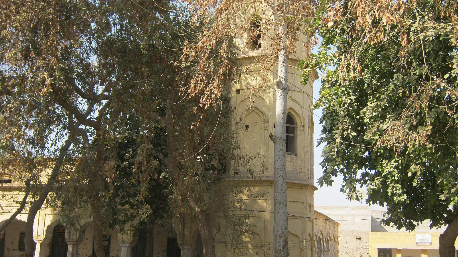 An old government school building with a tall tower, seen through trees