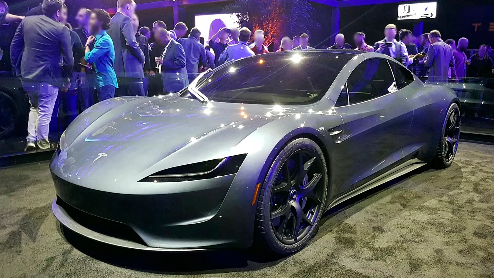 A silver Tesla Roadster prototype on display surrounded by people
